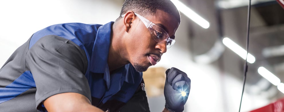 A Subaru technician using flashlight to look into a Subaru engine compartment. | Williams Subaru in Charlotte NC