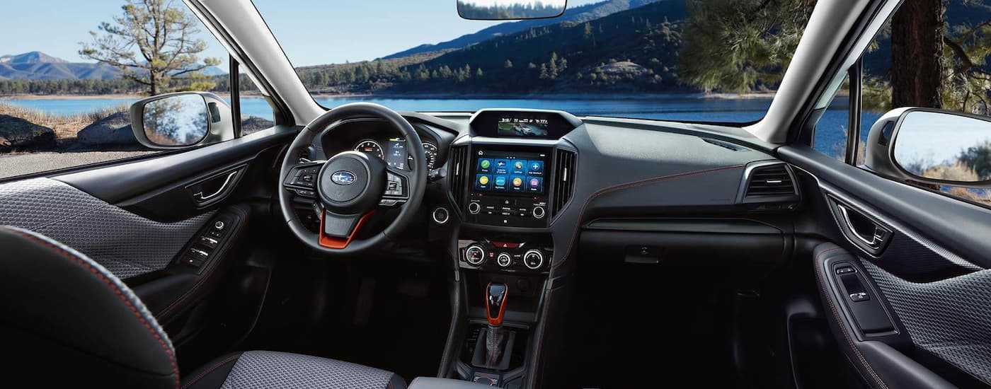 The front dash and interior in a 2022 Subaru Forester is shown overlooking a lake.