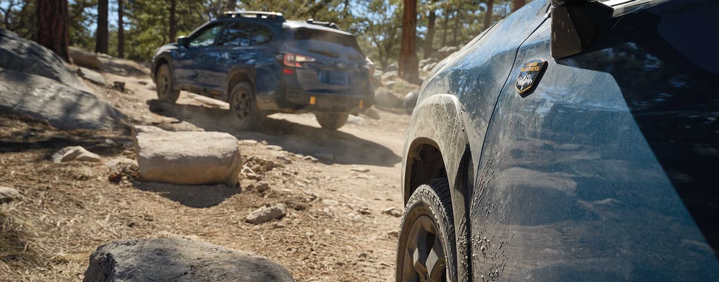 A blue 2022 Subaru Forester Wilderness is shown following an Subaru Outback on a dirt path.
