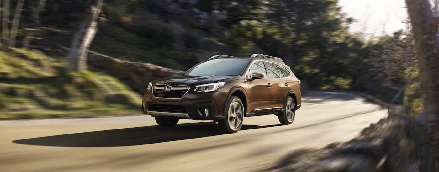 A brown 2022 Subaru Outback Touring is shown driving on a forest road.