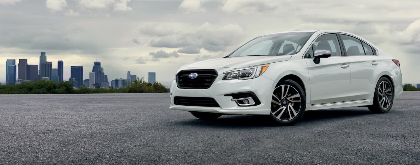 A popular Certified Pre-Owned Subaru, a 2019 Subaru Legacy Sport, is shown from the side with a city in the background.