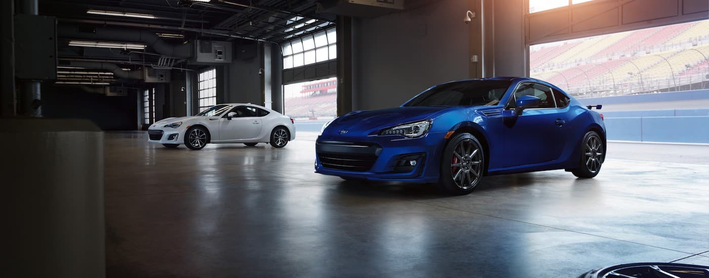 A blue and a white 2020 Subaru BRZ are shown parked in a large garage.