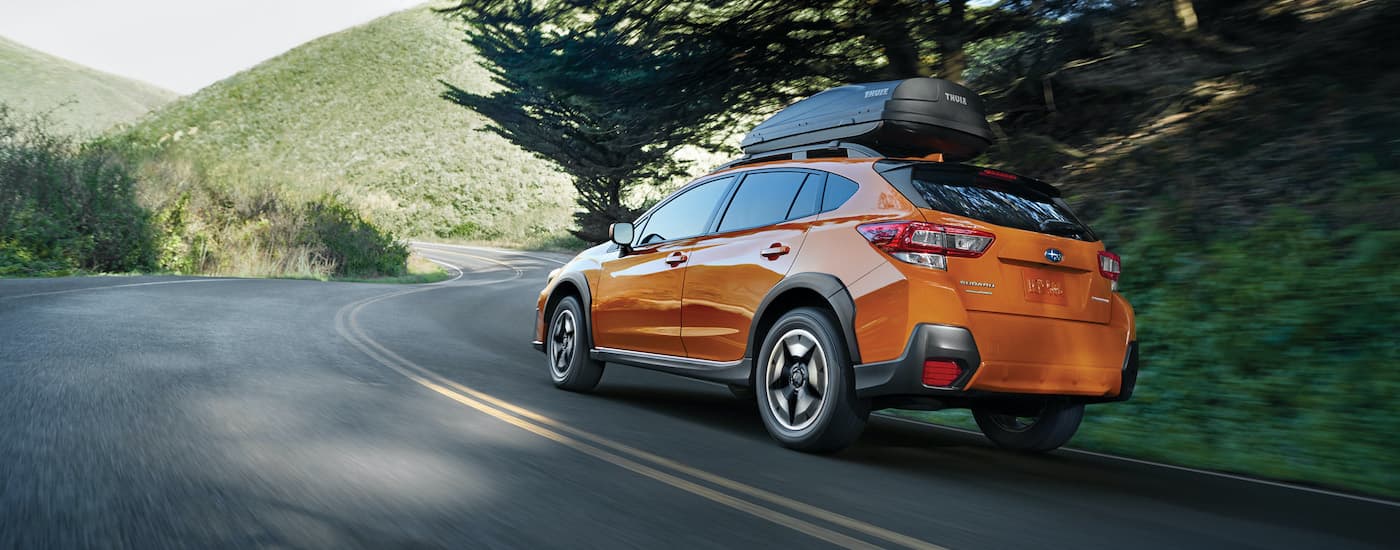 An orange 2020 Subaru Crosstrek Premium is shown from behind driving down a wooded road.