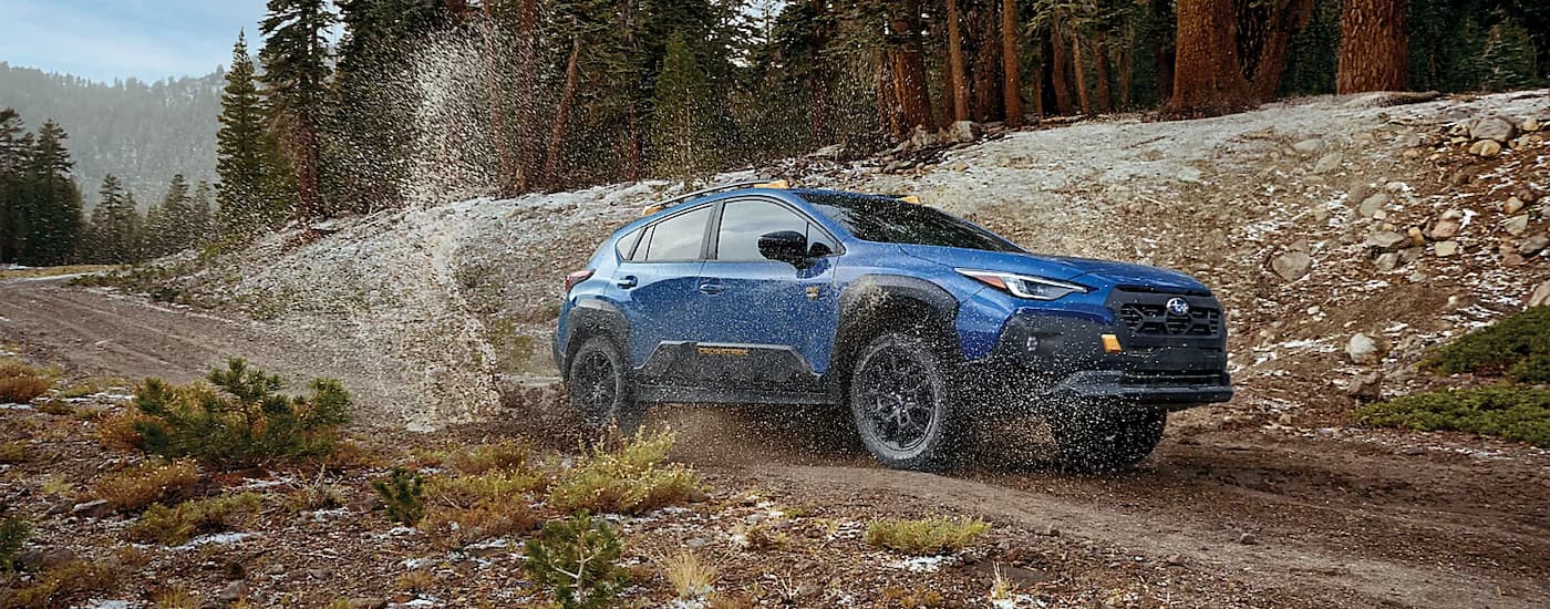 A blue 2024 Subaru Crosstrek Wilderness is shown driving through a muddy puddle on a dirt trail.