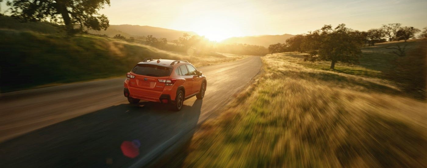 An orange 2018 Subaru Crosstrek Premium is shown driving on a sunny day.