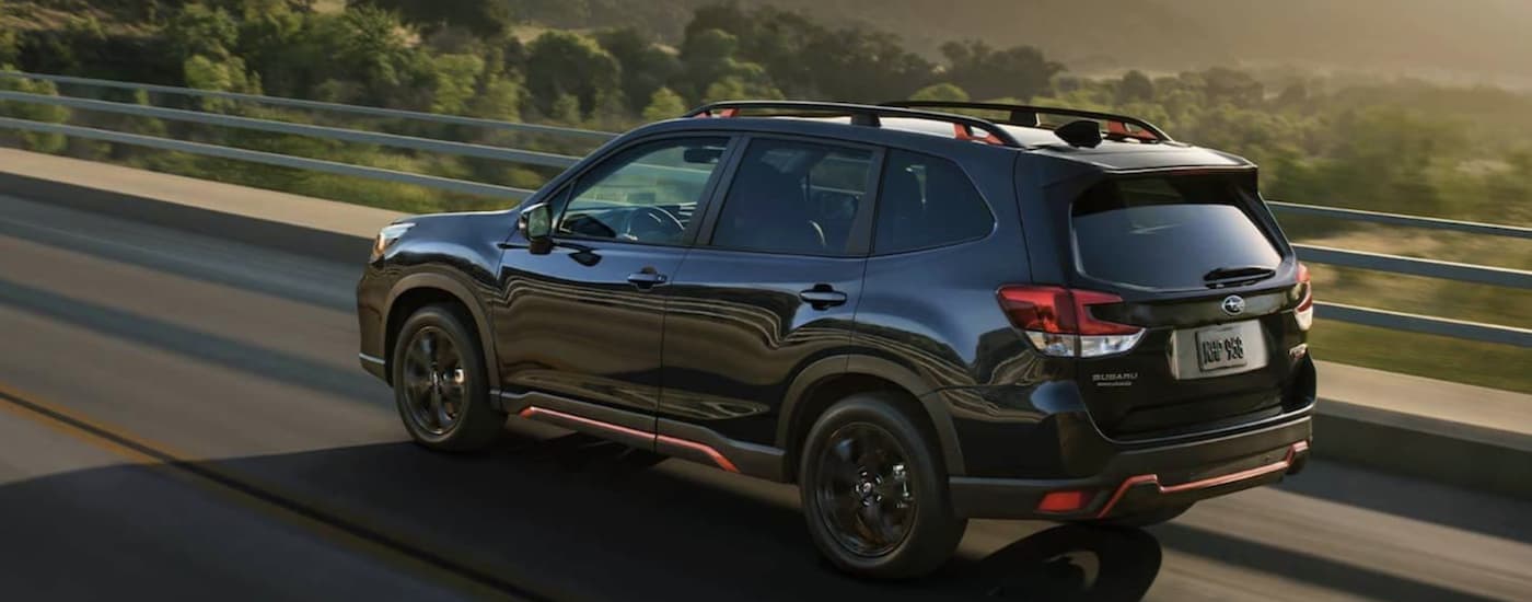 A black 2021 Subaru Forester is driving past mountains after leaving a Subaru Forester dealership.
