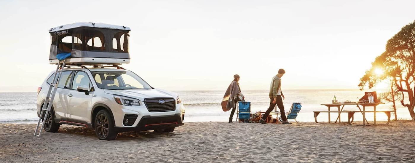 A white 2021 Subaru Forester with a roof tent is parked on a beach.