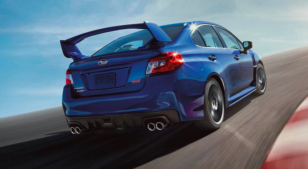 Rear view of a blue 2020 Subaru WRX STI rounding a corner at the racetrack.