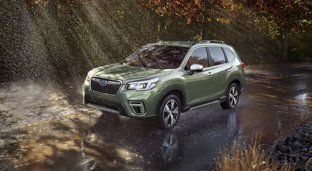 A green 2021 Subaru Forester driving through the rain in the woods.
