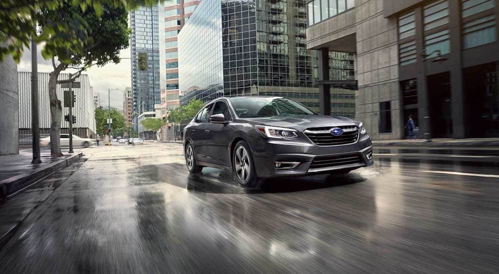 A grey 2021 Subaru Legacy driving on a wet city street after leaving a Subaru Legacy dealership.