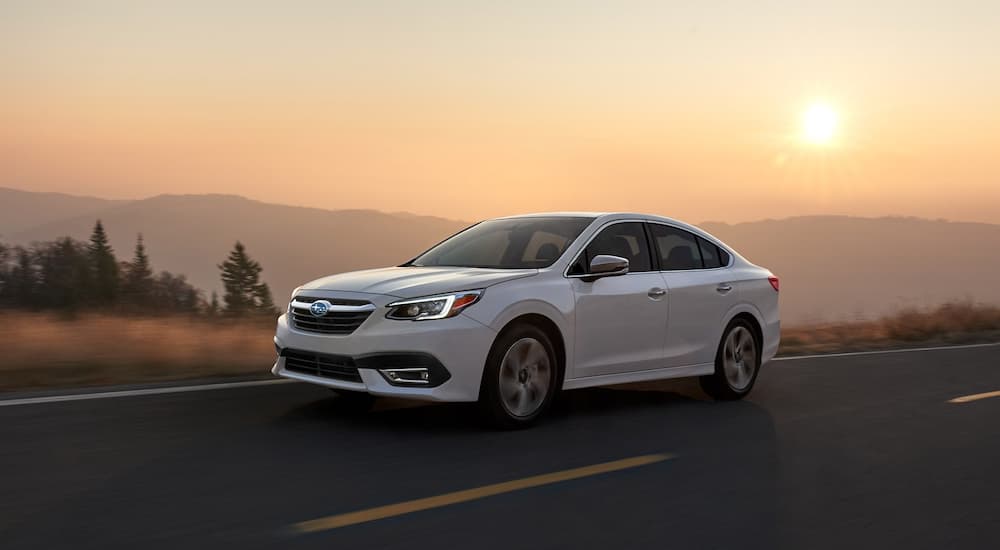 A white 2021 Subaru Legacy driving past mountains at sunset.