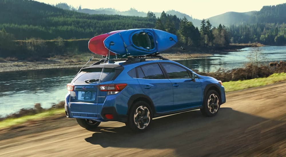 A blue 2021 Subaru Crosstrek Touring is shown from the side driving past a lake with kayaks on the roof.