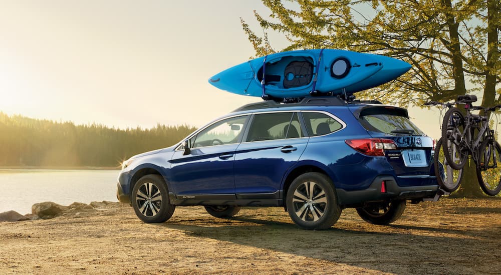 A blue 2019 Subaru Outback is shown next to a lake with a kayak on the roof.