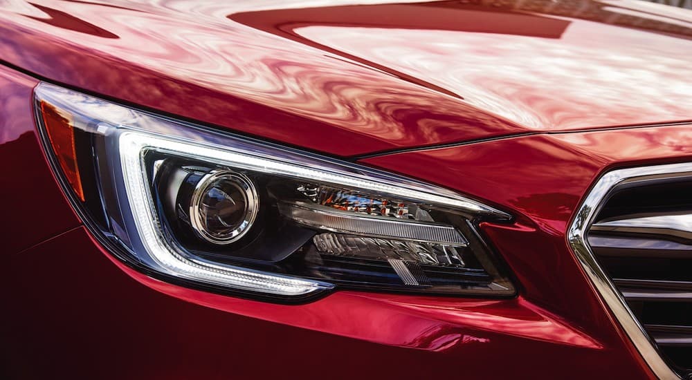 A close up shows the passenger headlight on popular Certified Pre-Owned Subaru Legacy, a red 2018 Subaru Legacy.