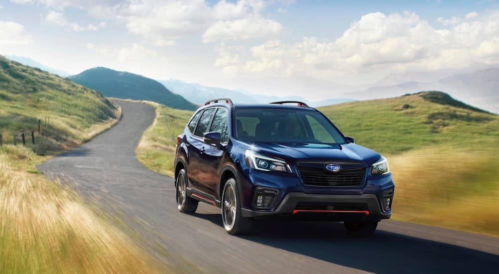 A black 2021 Certified Pre-Owned Subaru Forester is shown riving past rolling hills.
