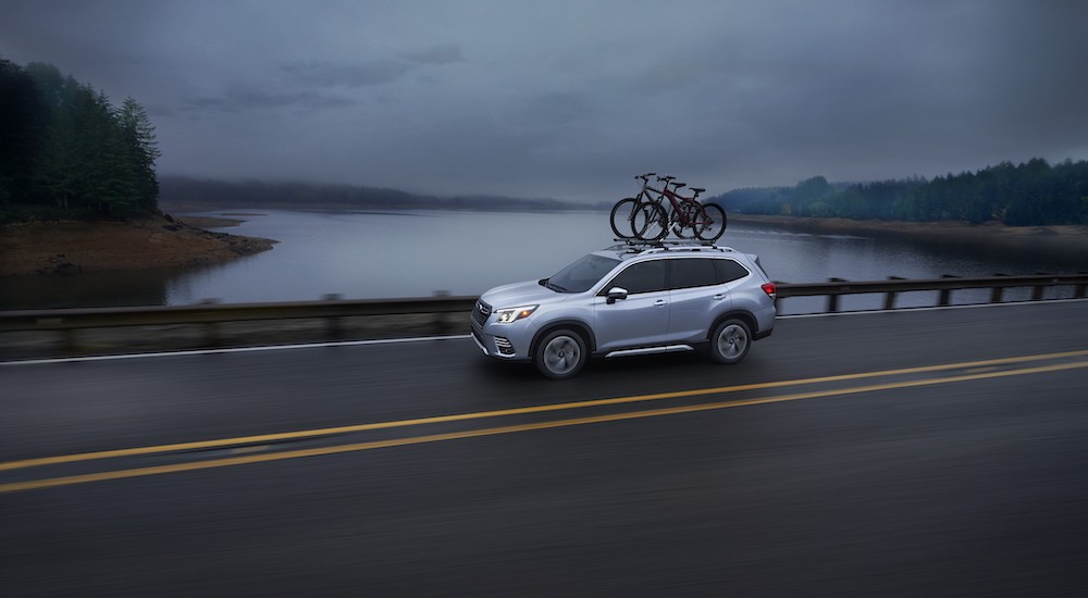 A silver 2022 Subaru Forester Touring is shown driving on a road next to a body of water.