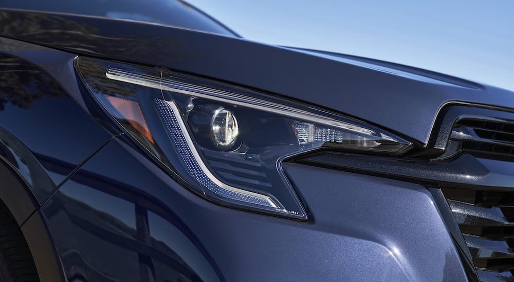 A close-up shows the passenger side headlight on a dark blue 2023 Subaru Ascent.