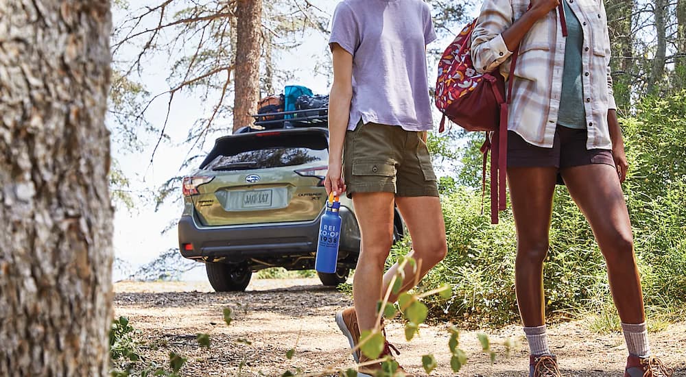 A green 2023 Subaru Outback is shown parked near hikers.