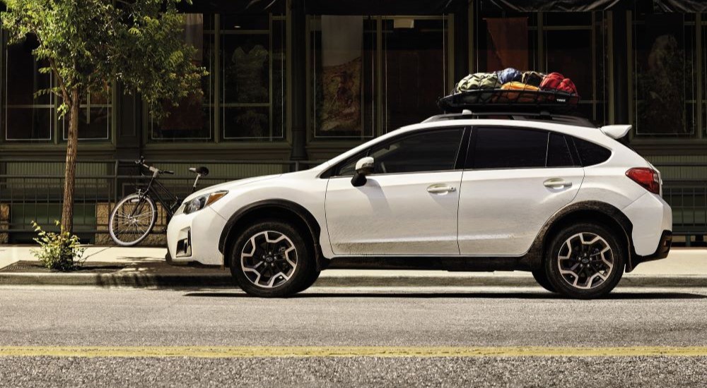 A popular Subaru SUV for Sale, a white 2016 Subaru Crosstrek, is shown from the side on a city street.