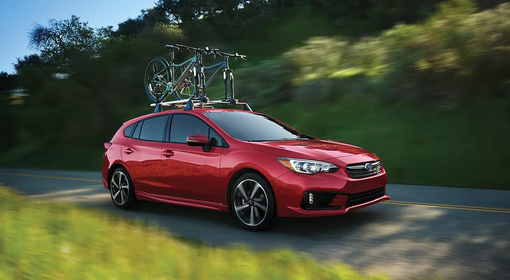 A red 2023 Subaru Impreza driving on an open road with bicycles on the roof
