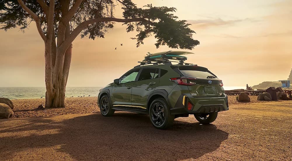 A green 2024 Subaru Crosstrek with surfboards on the roof rack, parked at the ocean.