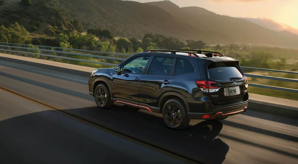 A black 2021 Subaru Forester driving on a highway with trees and mountains in the distance