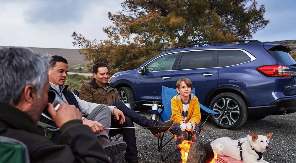 A family roasting marshmallows on a campfire near a blue 2024 Subaru Ascent 
