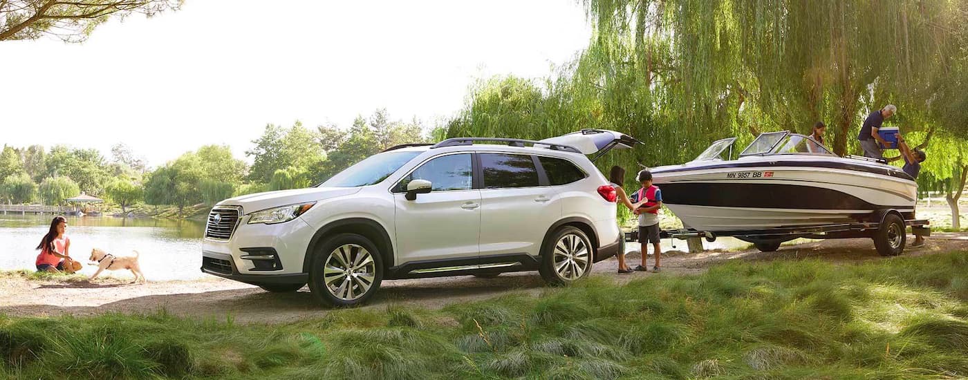A white 2022 Subaru Ascent Limited is shown from the side towing a boat next to a lake.