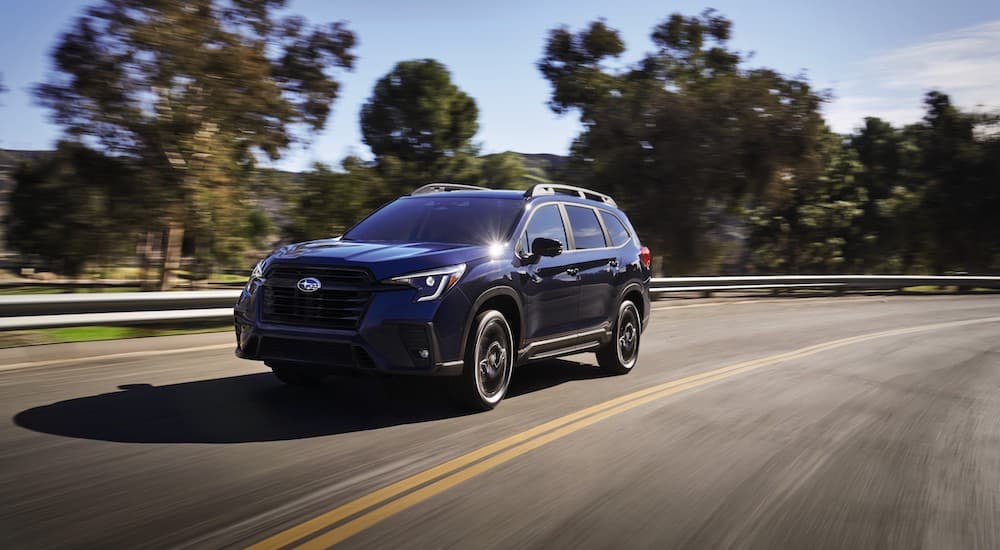 A blue 2023 Subaru Ascent driving on a tree-lined highway.