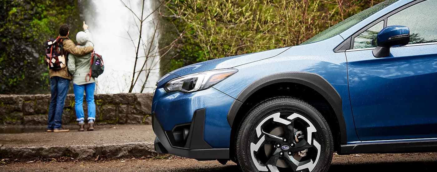A blue 2023 Subaru Crosstrek Limited parked near a waterfall as its passengers admire the view