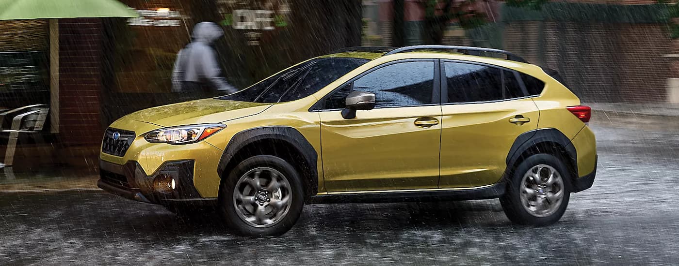 A gold 2023 Subaru Crosstrek driving on a city street in the rain