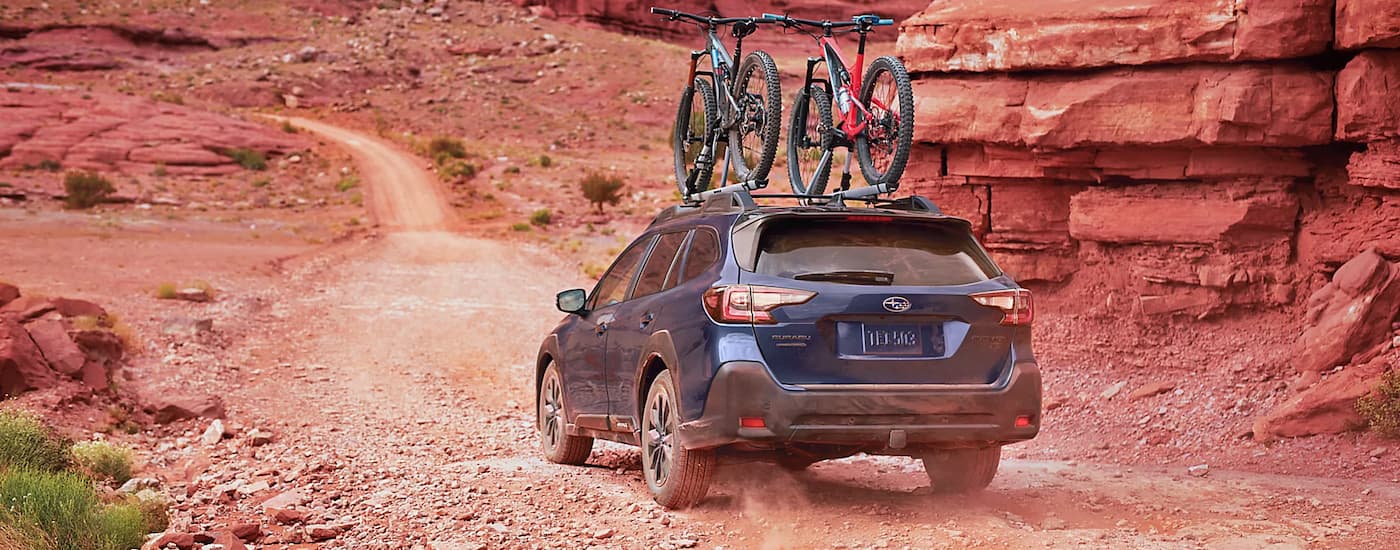 A blue 2022 Subaru Outback with bikes on the roof, driving on a dusty desert trail