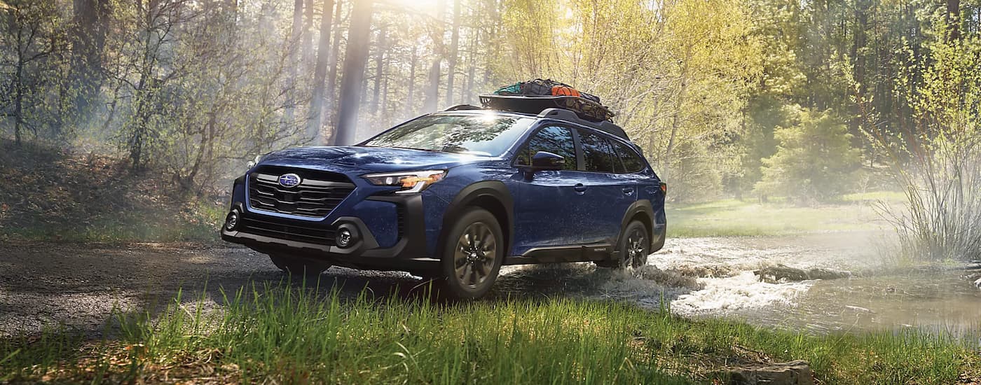 A blue 2022 Subaru Outback Onyx Edition driving through a small brook in the woods.
