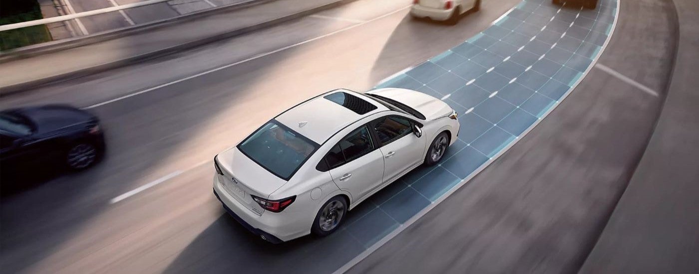 Overhead view of a white 2024 Subaru Legacy driving on a multi-lane road with simulated sensor lines.