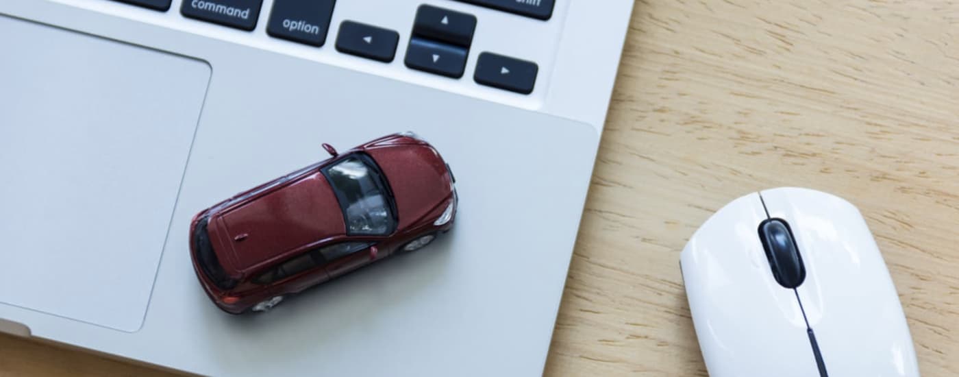 A red toy car is shown on a laptop keyboard next to a mouse.