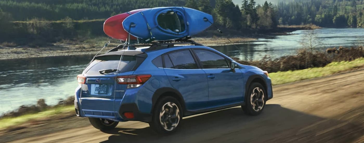 A blue 2021 Subaru Crosstrek is shown from the rear driving near a body of water.