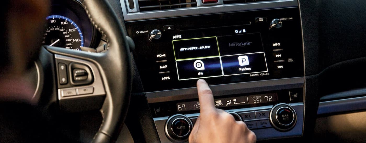 A close up shows a person about the touch the Starlink app in a 2016 Subaru Legacy.