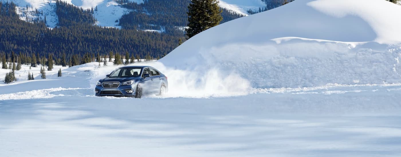 A blue 2019 Subaru Legacy is shown kicking up snow on a winter trail.