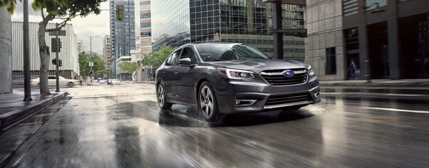 A grey 2021 Subaru Legacy Limited is shown driving through a city after leaving a Certified Pre-Owned Subaru Legacy dealership.