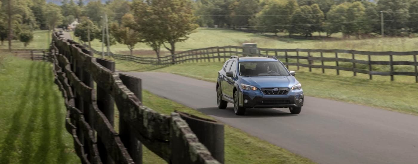 A blue 2021 Subaru Crosstrek Sport is shown driving past a field and a fence.