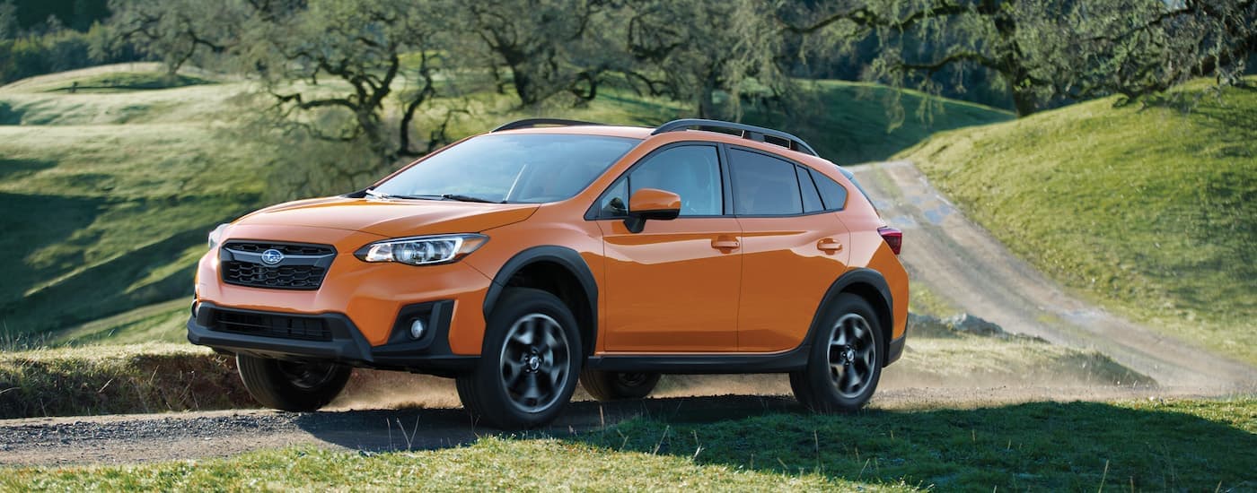 An orange 2019 Subaru Crosstrek is driving on a rural dirt road.