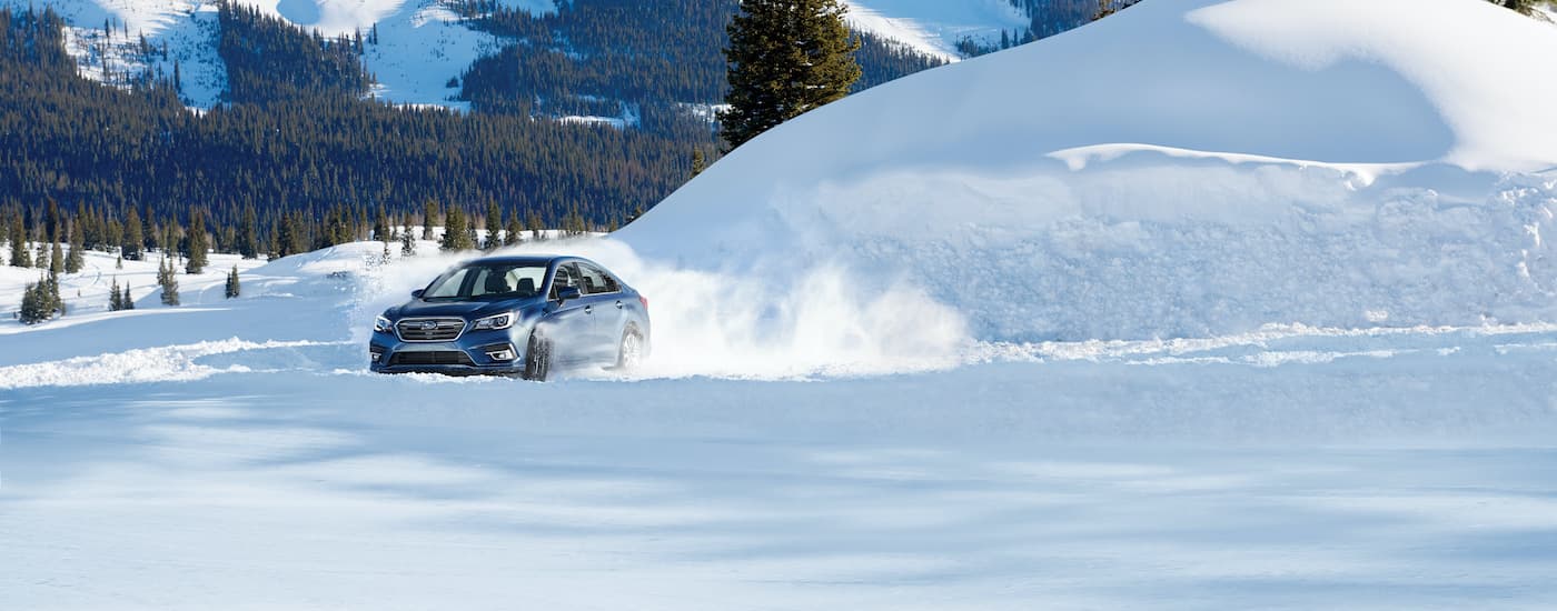 A blue 2019 Subaru Legacy is shown kicking up snow on a mountain road.