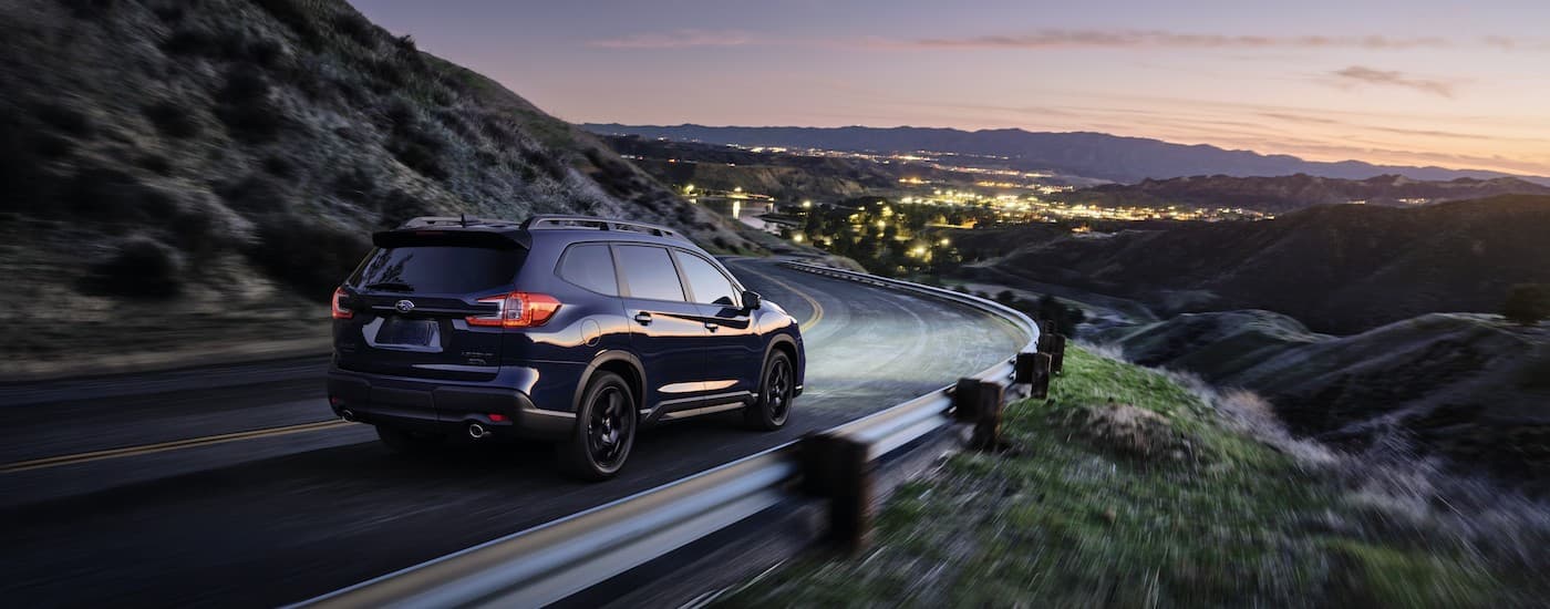 A black 2023 Subaru Ascent is shown from the rear driving toward a city at night.