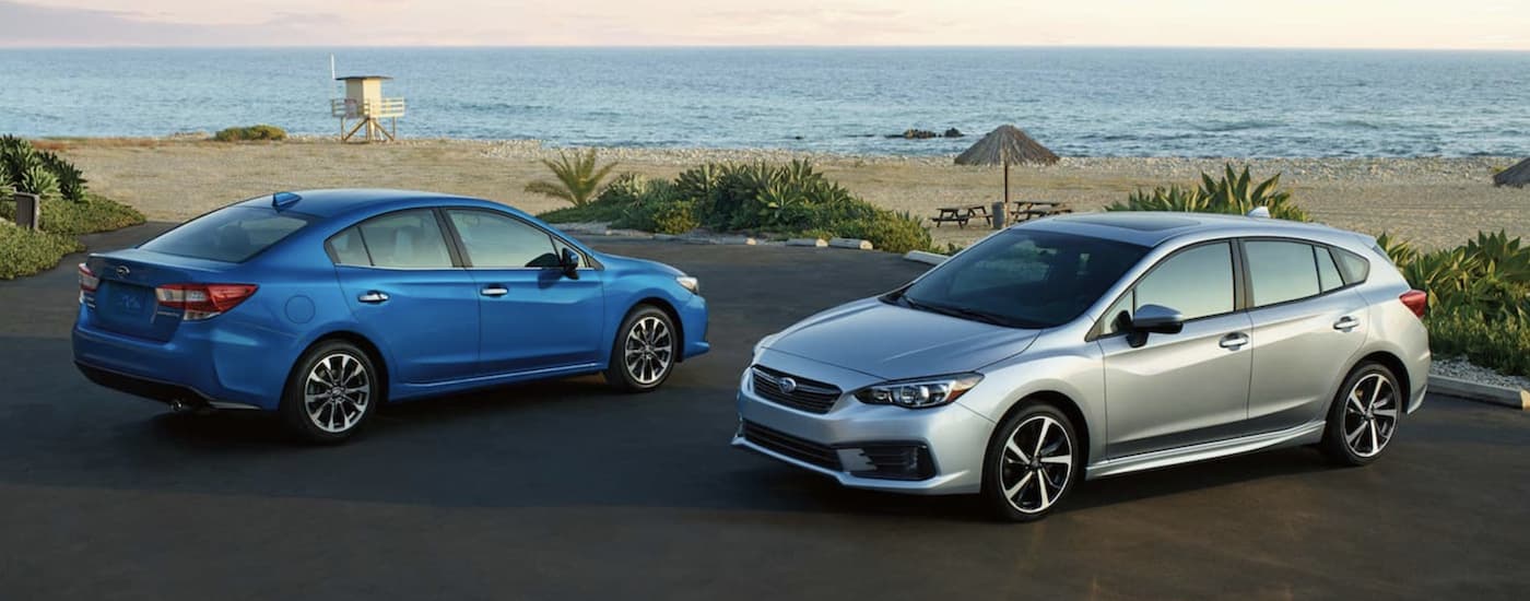 A blue 2021 Subaru Impreza and a silver Impreza hatchback are parked at the beach.