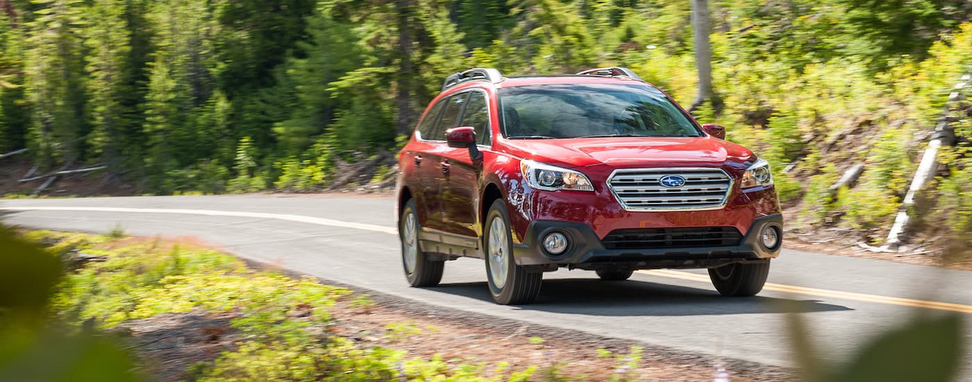 A red 2015 Subaru Outback is shown driving on a tree-lined road.