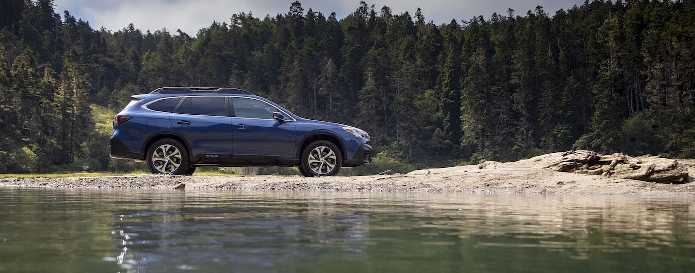 A blue 2020 Subaru Outback is shown from the side parked next to a lake.