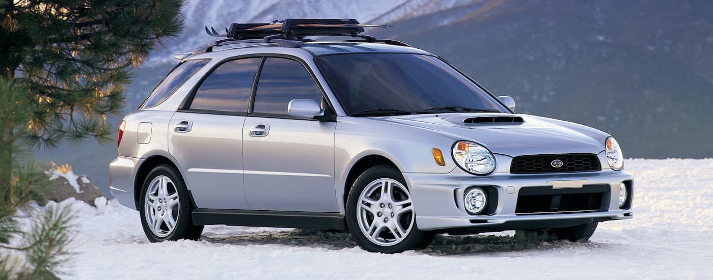 A silver 2002 Subaru WRX is shown from the side with snowboards on the roof.