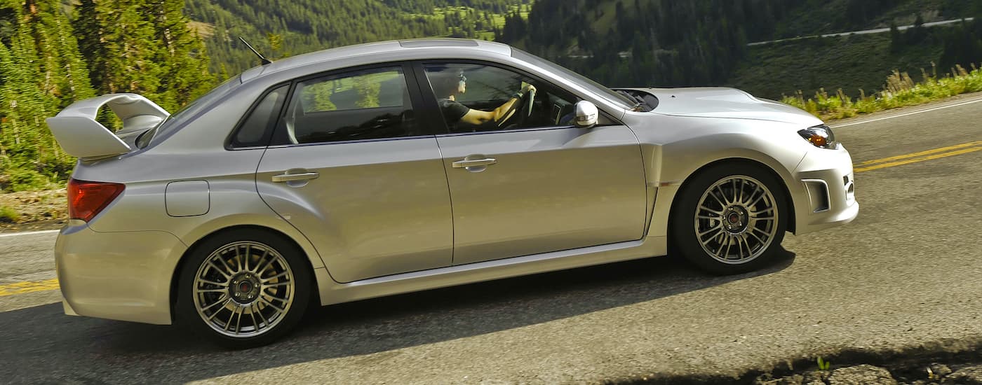 A silver 2012 Subaru WRX STI is shown from the side driving on a mountain road.