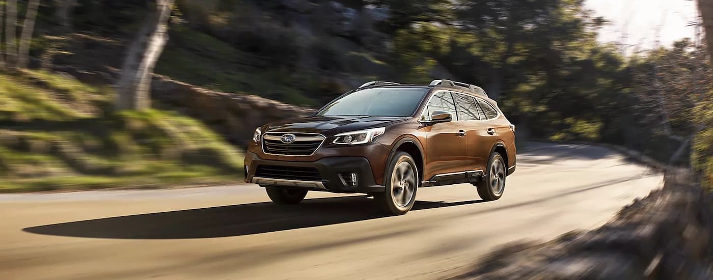 A brown 2022 Subaru Outback Touring is shown driving on a tree-lined road after viewing used Subarus for sale.