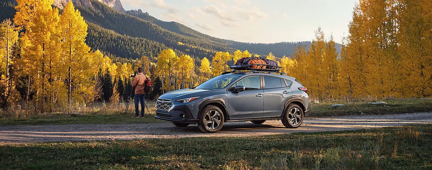 A grey 2024 Subaru Crosstrek is shown from the side overlooking a mountain view.